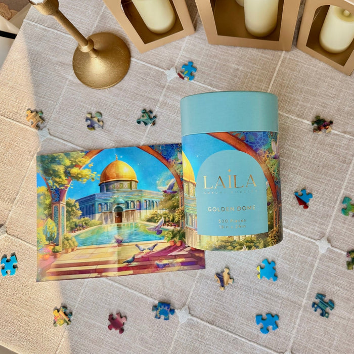 A Laila Luxury Puzzles Golden Dome 500-piece jigsaw puzzle sits on a table beside a Palestine puzzle guide with a dome illustration, surrounded by loose pieces from the Ola El-Metwally design.