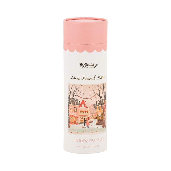 A cylindrical container with a pink lid labeled "Love Found Here | 300 Piece Jigsaw Puzzle" by My Mind's Eye, featuring a village couple illustration—an ideal romantic puzzle and perfect gift for couples.