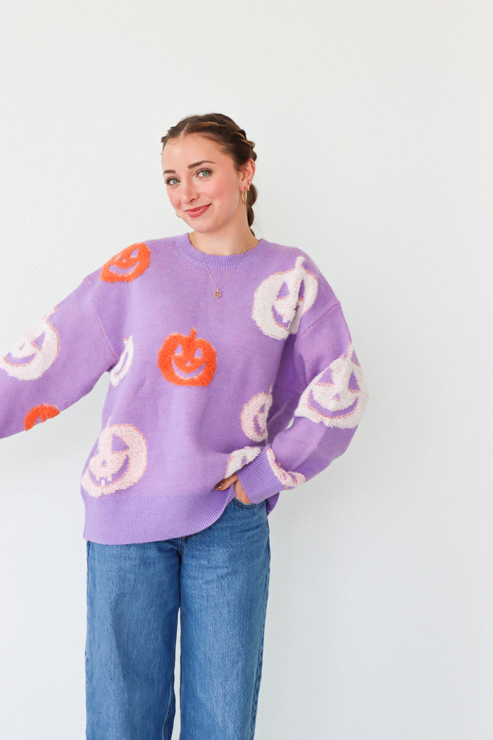 Person wearing a purple Halloween-themed sweater with pumpkins and ghosts on a white background